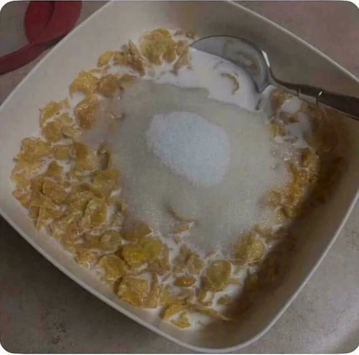 A bowl of corn flakes cereal with milk and a large spoonful of sugar from the 90s.