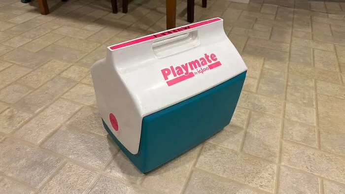 A vintage blue and white Igloo Playmate cooler from the 90s sitting on a tiled kitchen floor
