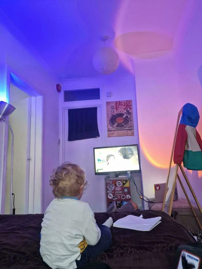A toddler watching television in a bedroom illuminated by colorful mood lighting, from wholesome pics of dads.