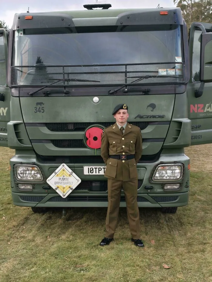 A proud military dad standing in uniform in front of a green army truck, capturing wholesome pics of dads.