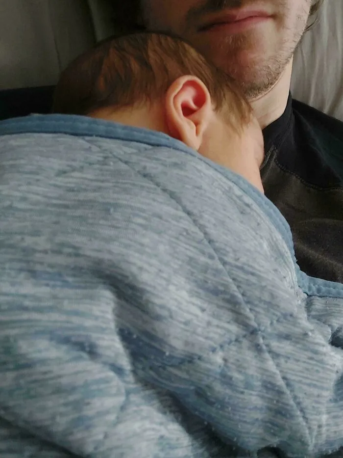 A sleeping baby cradled against a father chest, representing wholesome dads practicing fatherhood.