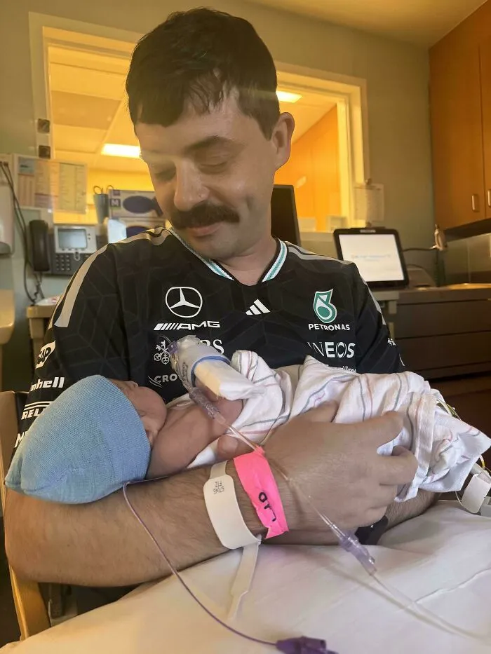 A proud dad with a mustache holding his newborn baby in a hospital room, capturing wholesome pics of dads