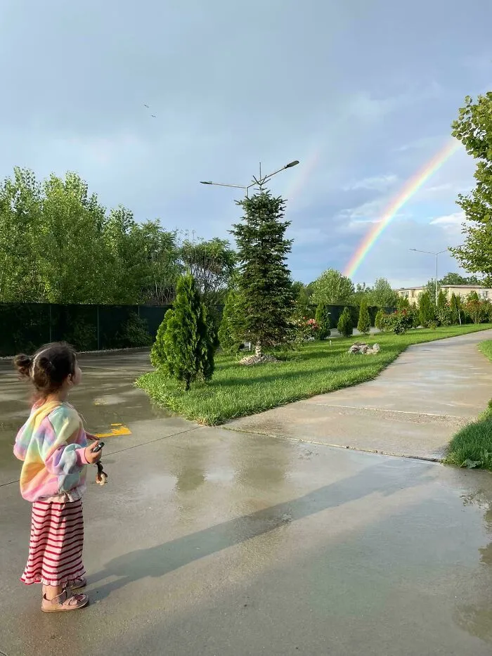 A young girl in colorful clothes admiring a rainbow outdoors, illustrating wholesome pics of dads and wholesome parenting