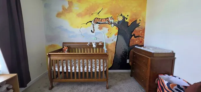 A warm nursery with a Calvin and Hobbes mural painted on the wall, showing dads nailing fatherhood.