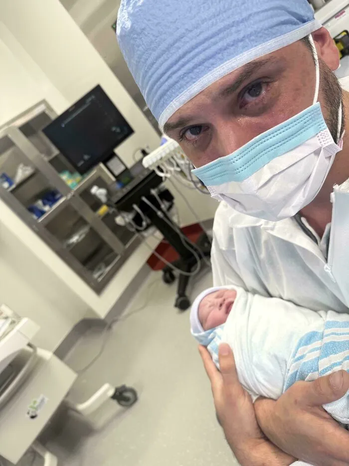 An emotional dad in hospital scrubs holding his newborn baby in a wholesome moment