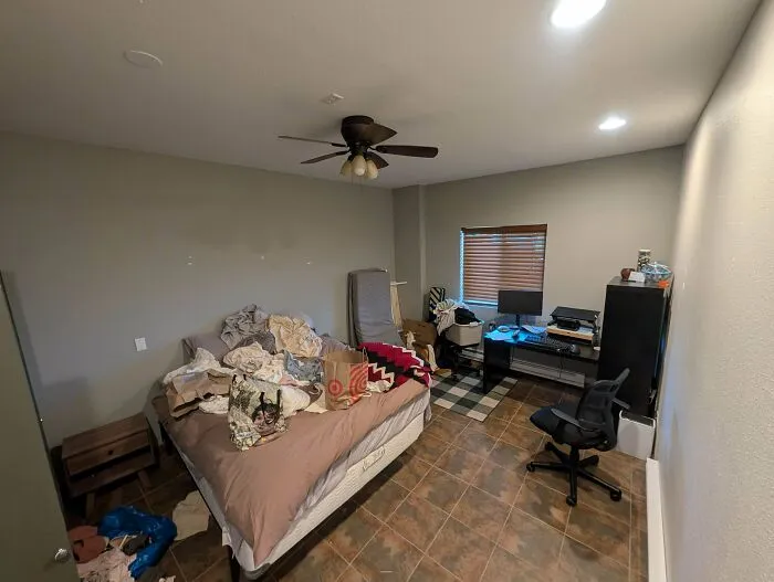 A bedroom with an unmade bed, bags, and a home office desk setup for wholesome dad life.
