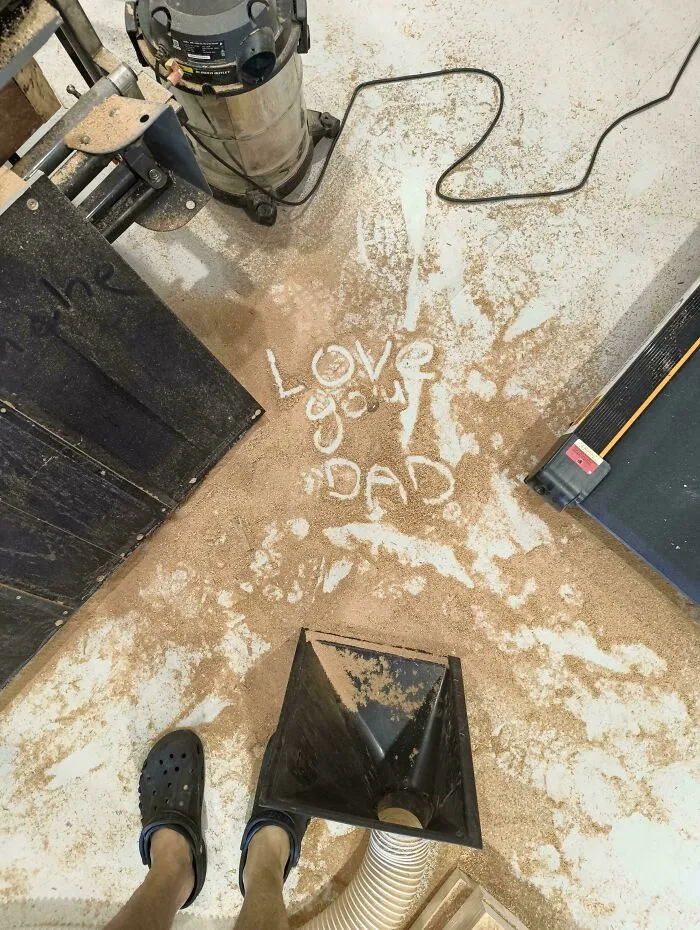 Sawdust on a workshop floor written with the message Love you dad next to woodworking tools.