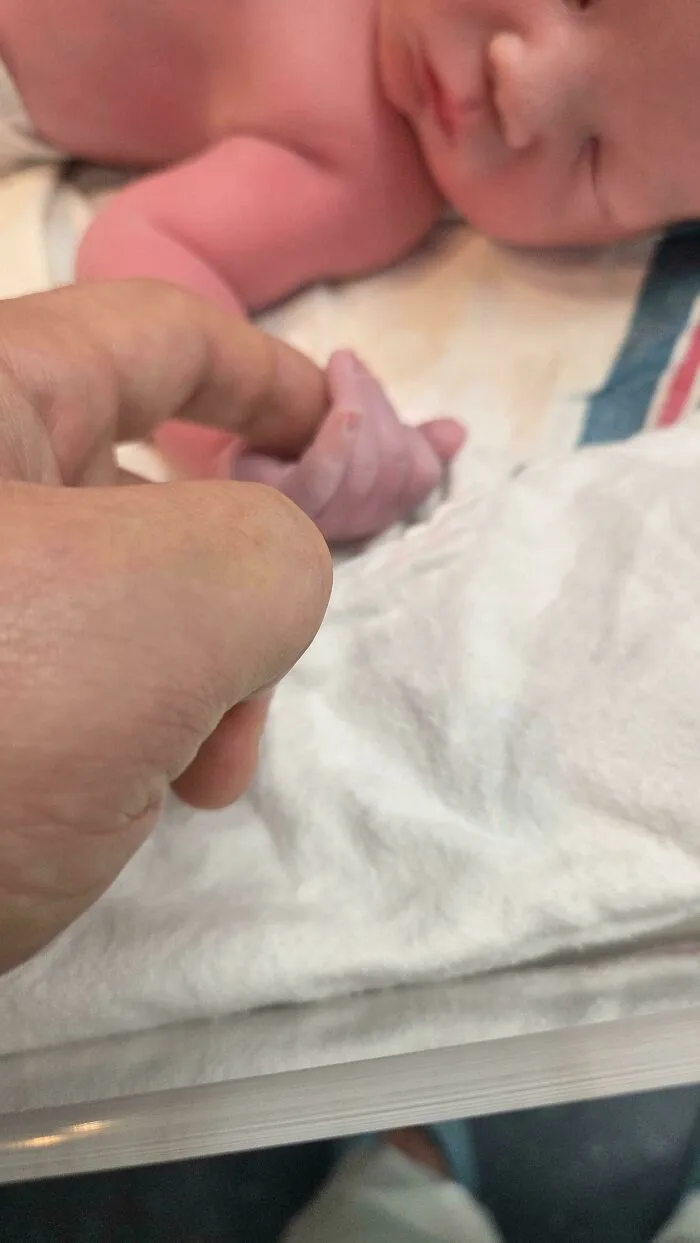 A newborn baby holding a father finger in a hospital, featured in wholesome pics of dads.