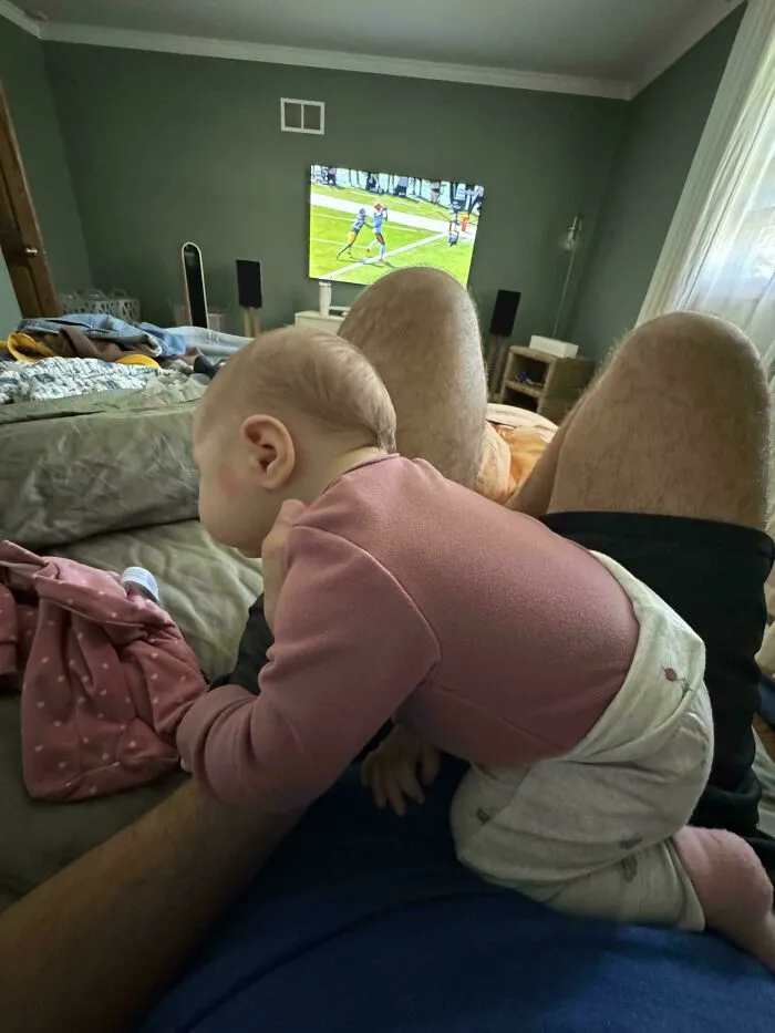 A baby resting on dad while watching football on TV, showcasing wholesome pics of dads.