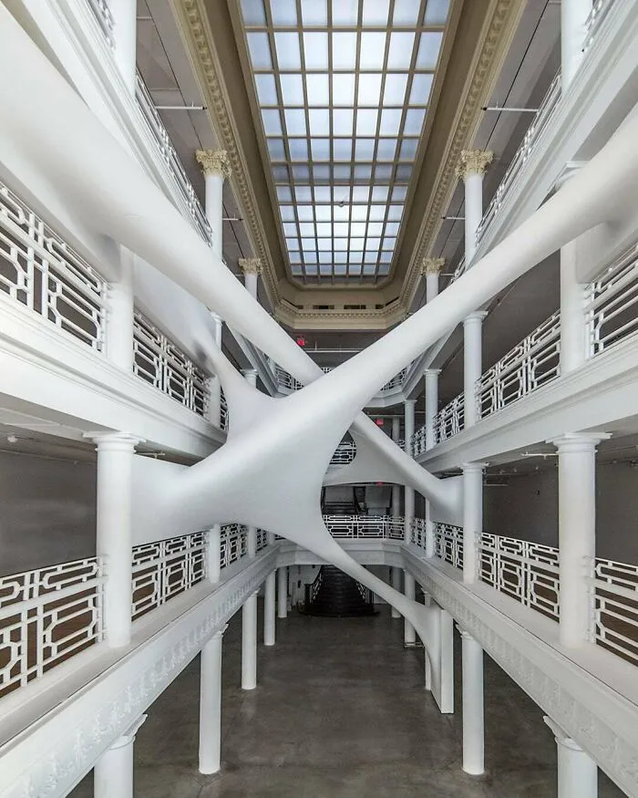 Surreal white organic sculpture installed inside a multi-story atrium among architectural masterpieces