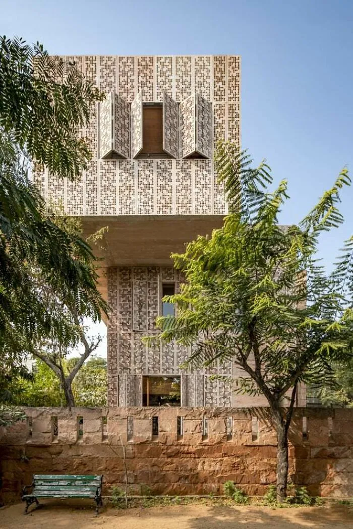 A modern perforated stone structure displaying unique architectural masterpieces in a garden setting.