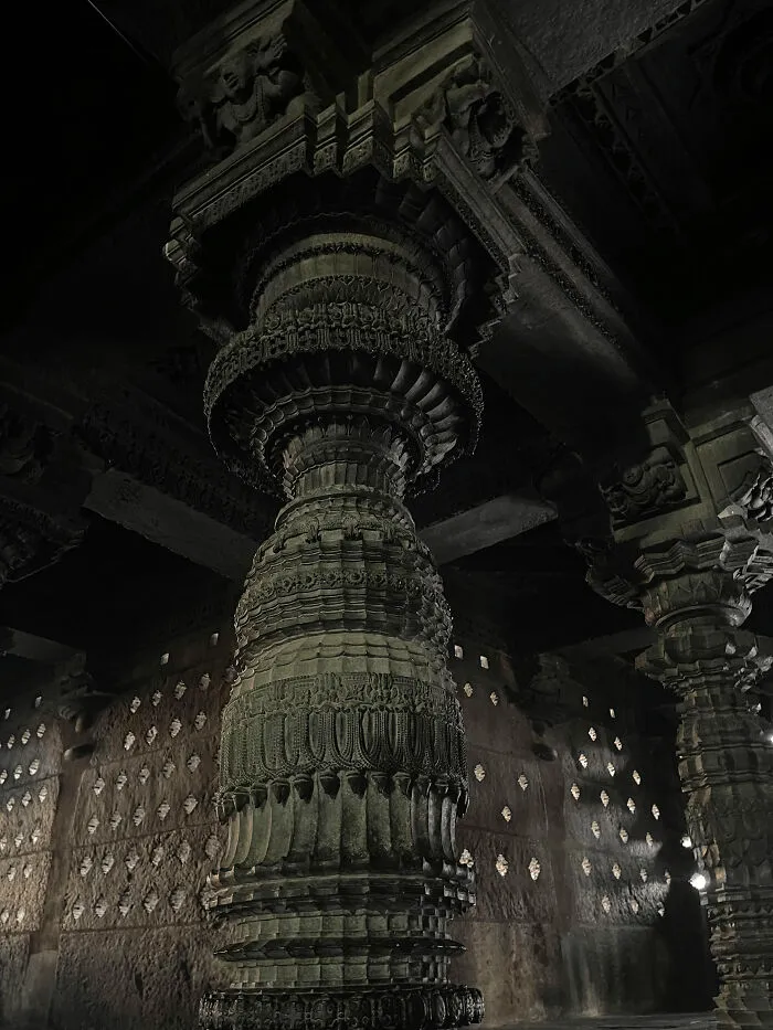 Dramatically lit stone pillar with detailed carvings representing ancient architectural masterpieces
