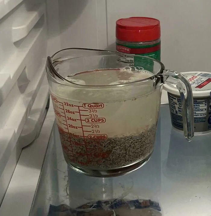 A glass measuring cup storing oats soaking in liquid inside a refrigerator showcasing frugal tips.