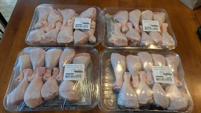 Four plastic trays filled with raw chicken drumsticks showing frugal tips for buying in bulk