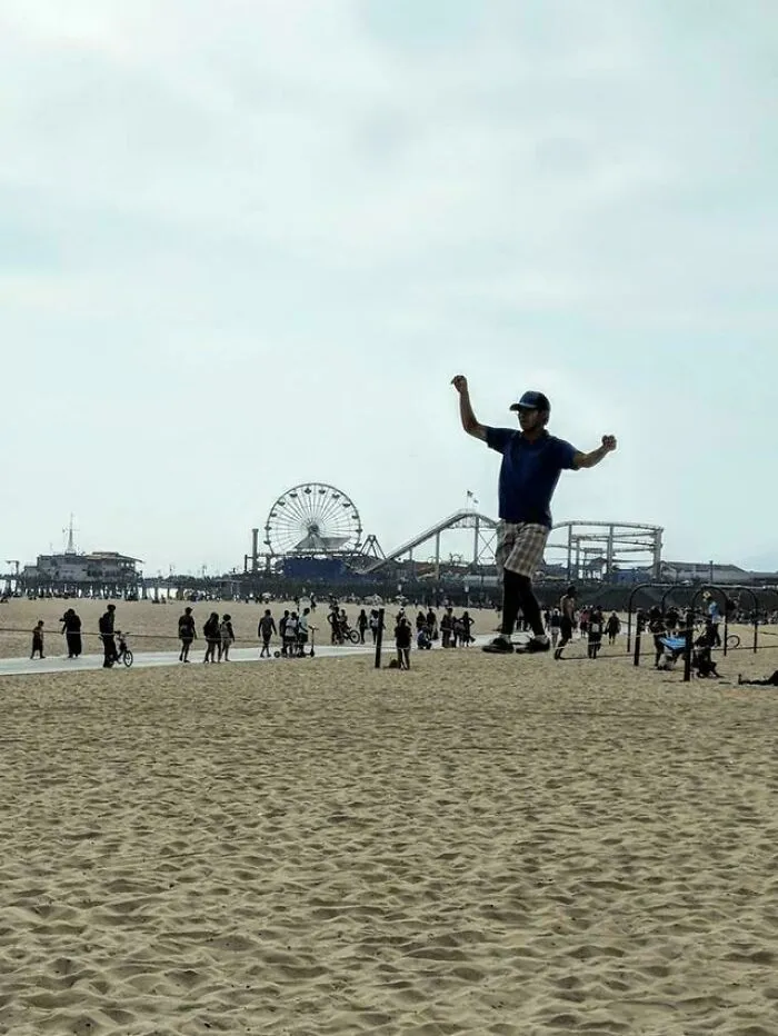 Man walking on slackline above sand at beach with amusement park in background