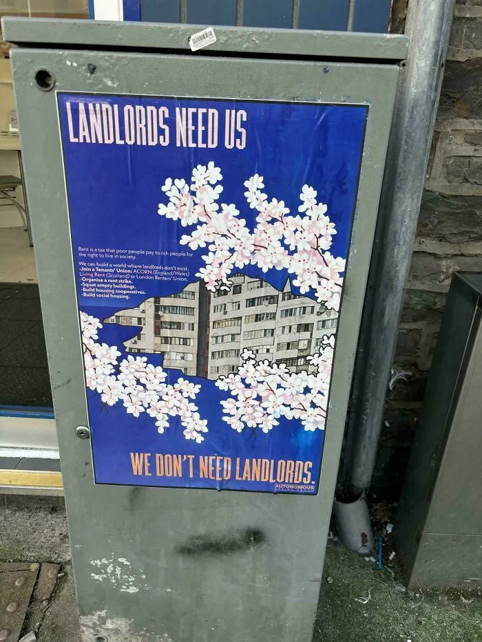 Protest poster stating Landlords Need Us, We Don't Need Landlords, taped to a utility box.