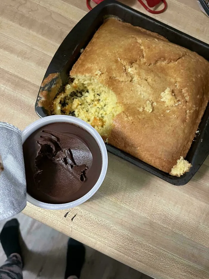 A baked cake in a pan with a corner dug out next to frosting, capturing the sheer audacity of dessert thieves.