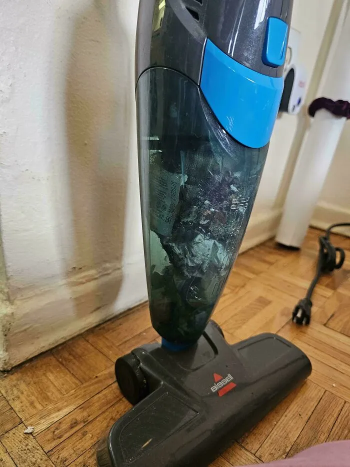 An overfilled vacuum canister packed with debris, showcasing sheer audacity of chores left undone.