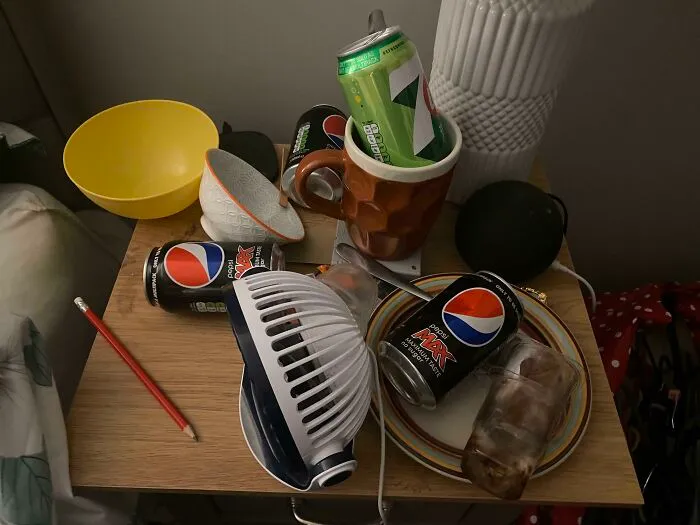 A messy bedside table covered in empty soda cans, demonstrating sheer audacity in a shared home.