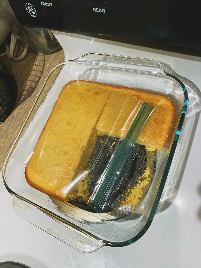 Cornbread in a glass pan with a plastic bag placed carelessly over it showing the sheer audacity of some men