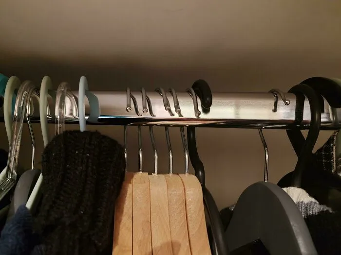 Wooden and plastic clothes hangers arranged incorrectly on a closet rod, showing sheer audacity