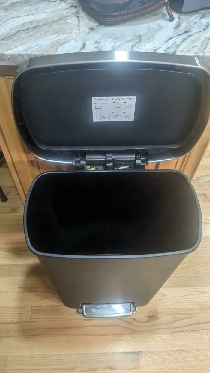 An empty black trash can on a wooden floor, symbolizing the sheer audacity of undone chores
