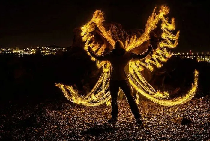 A person with fire wings standing on rocks, a real picture that looks too perfect to be natural