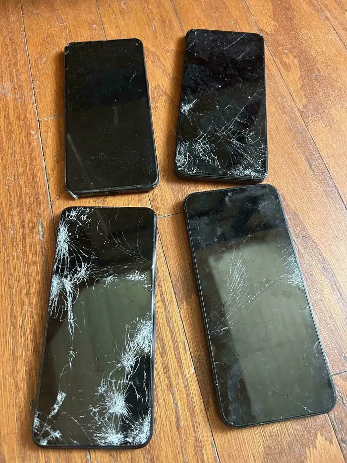 Four smartphones with cracked screens on a wooden floor showing funny quirks of a husband