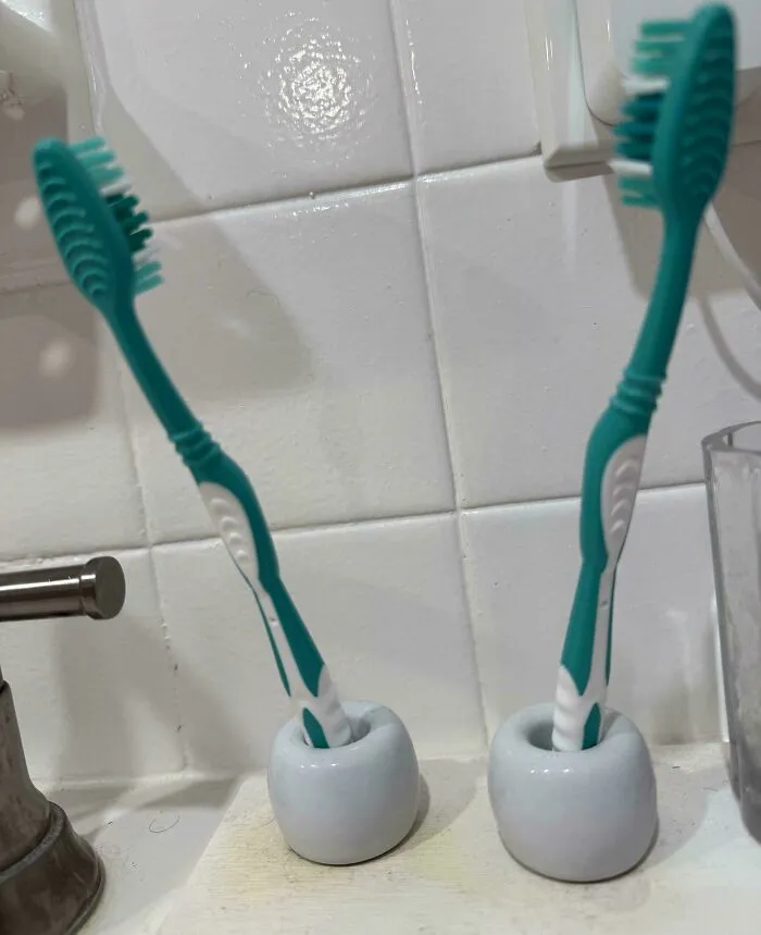 Two matching green and white toothbrushes in holders on a bathroom sink, representing a husband's quirky habits