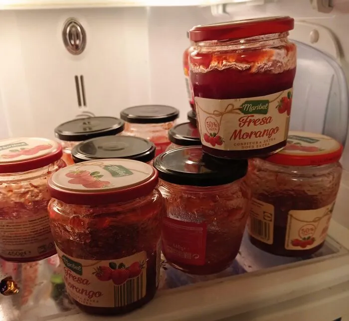 A fridge door stuffed full of opened, half-empty strawberry jam jars, showcasing sheer audacity