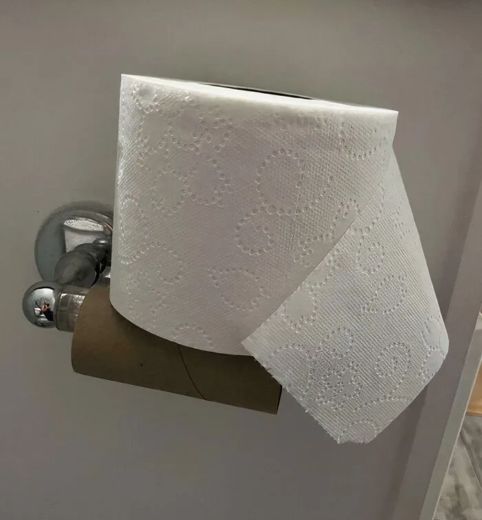 A new roll of toilet paper sitting on top of an empty cardboard roll on a dispenser, depicting male audacity
