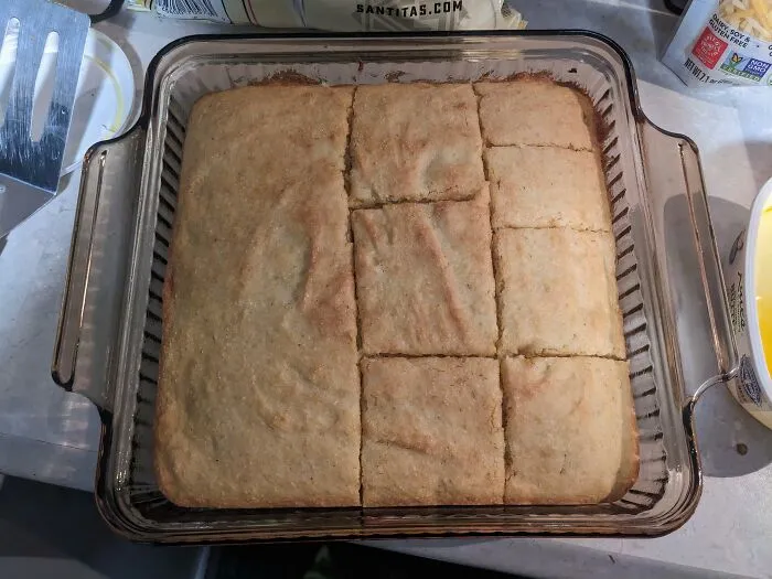 A freshly baked cornbread in a glass dish unevenly sliced, highlighting sheer audacity in food presentation