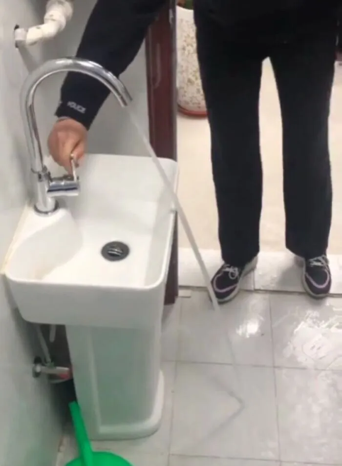 Poorly placed faucet spraying water onto the floor from a small bathroom pedestal sink.