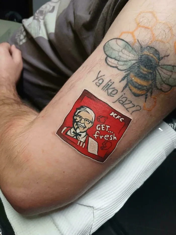 An arm tattoo featuring a bee and Colonel Sanders logo, examples of awful to look at creations.