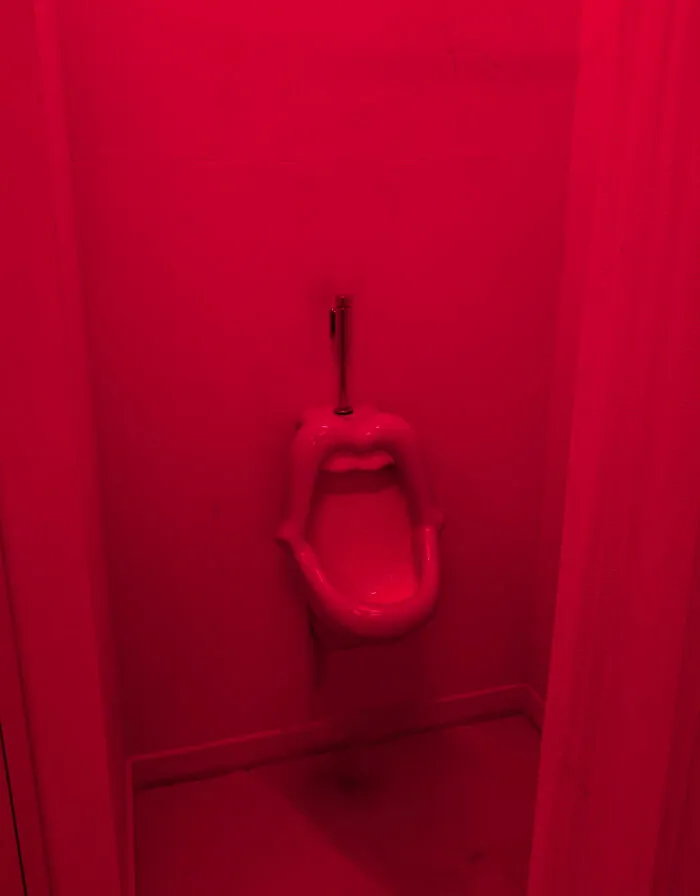 A lip-shaped red urinal mounted on a wall under red lighting, an example of awful creations in design.