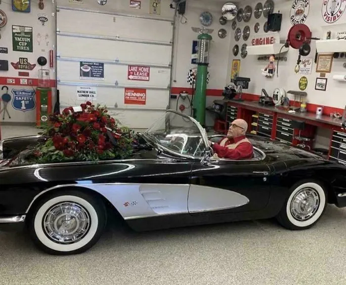 A classic convertible sports car in a garage with red flowers on the hood, one of many awful creations.