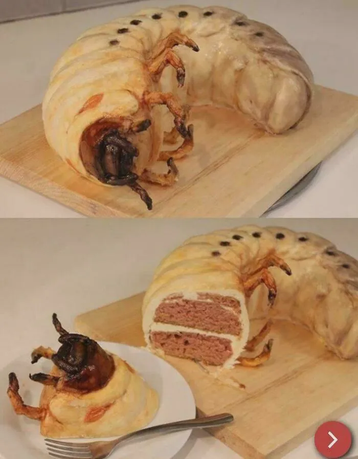 A realistic giant grub cake creation, well-made yet awful to look at, sliced open on a board.