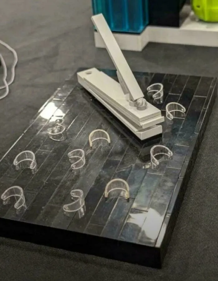 Realistic glass or metal sculpture of a giant nail clipper holding false nails among creations awful to look at.