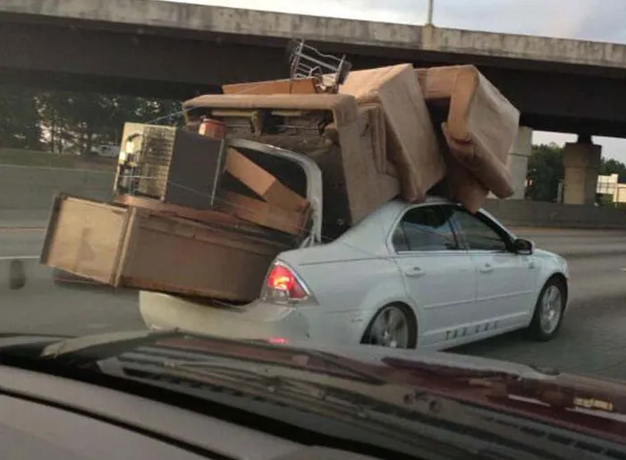 Sedan overloaded with furniture on roof and trunk depicts moving fails