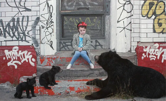 A girl sits on graffiti-covered steps near a black bear and cubs in dystopian paintings by Kevin Peterson.