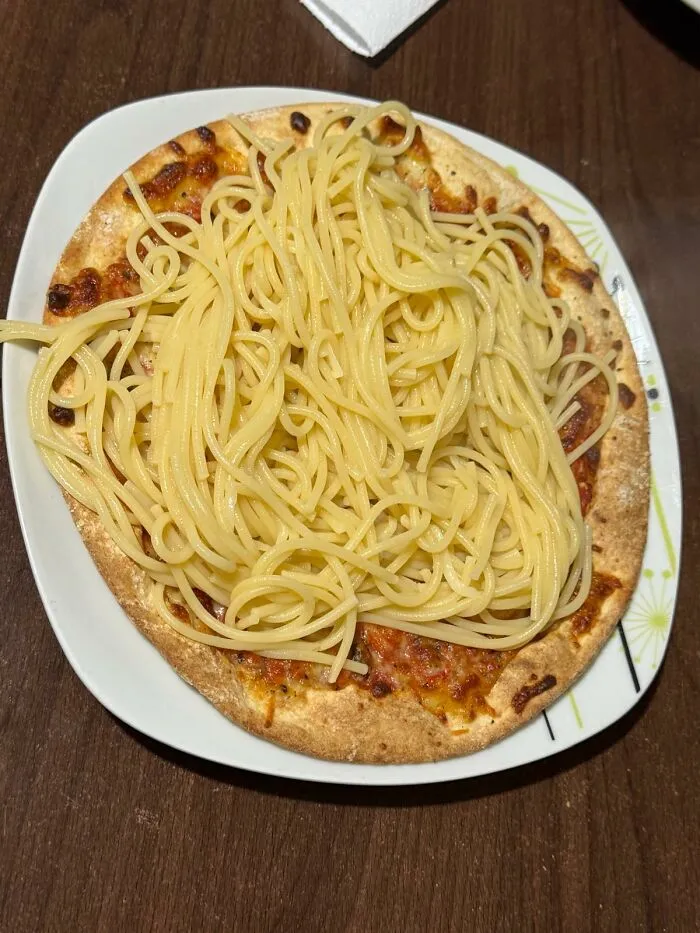 Unique food combinations featuring a plain cheese pizza topped with a mountain of plain cooked spaghetti noodles
