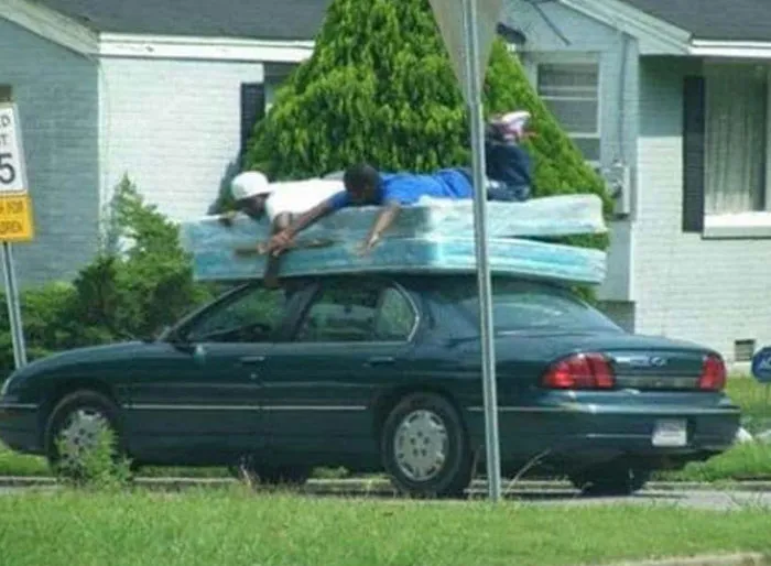 Car carrying mattress with person lying on top illustrates moving fails