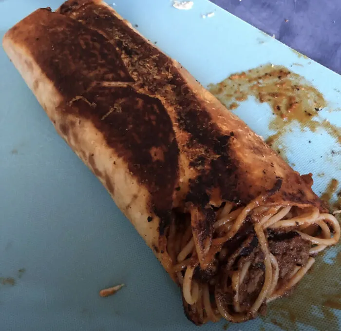 A toasted burrito filled with spaghetti and meat sauce, illustrating odd food combinations