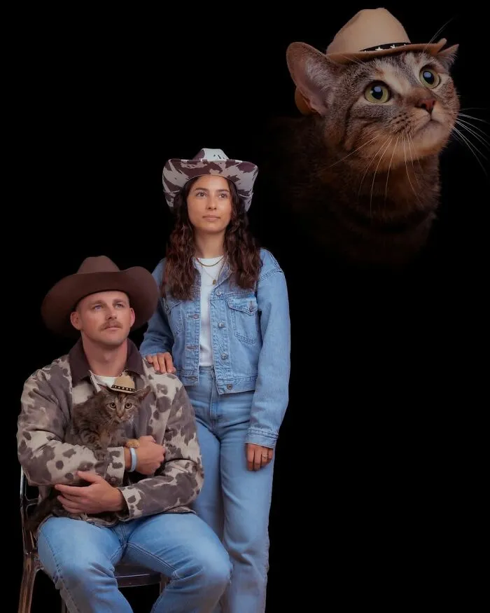 Silly portrait of a couple in cowboy hats and denim, with their cat wearing a matching hat, against a dark background.