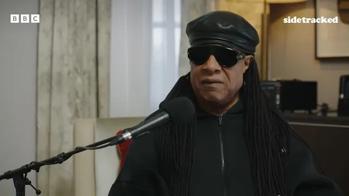 Stevie Wonder speaking at a microphone, illustrating stories of historical medical practices.