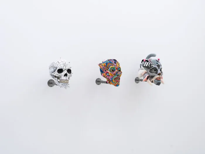 A gallery view of three unusual sculptures including a grid skull and vibrant thread-wrapped heads