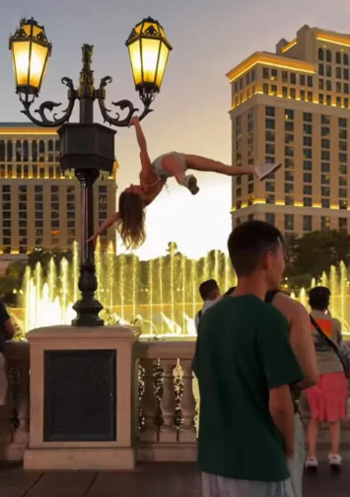 A main character woman hangs sideways from a lamppost over a fountain.