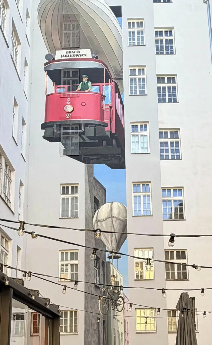 Mural of a red tram flying next to a building that might make you look twice to believe it.