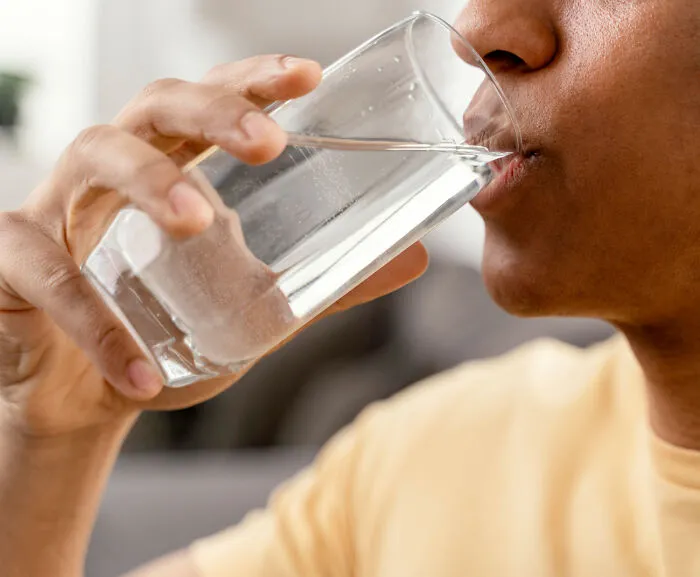 A person drinking water from a clear glass, highlighting potential problems with resource access in society.