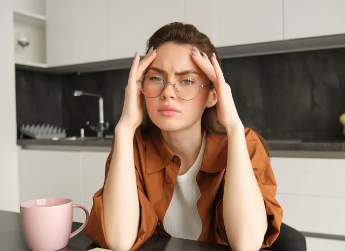 A stressed young woman with her hands on her head in a kitchen, showing the stress felt by divorced people
